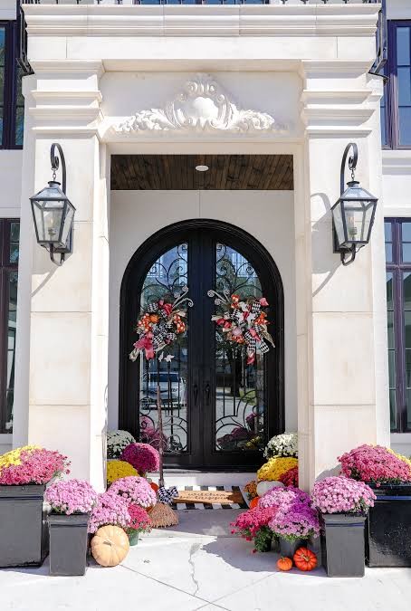 Autumn entrance with pink and yellow chrysanthemums, pumpkins and wreaths on black double doors